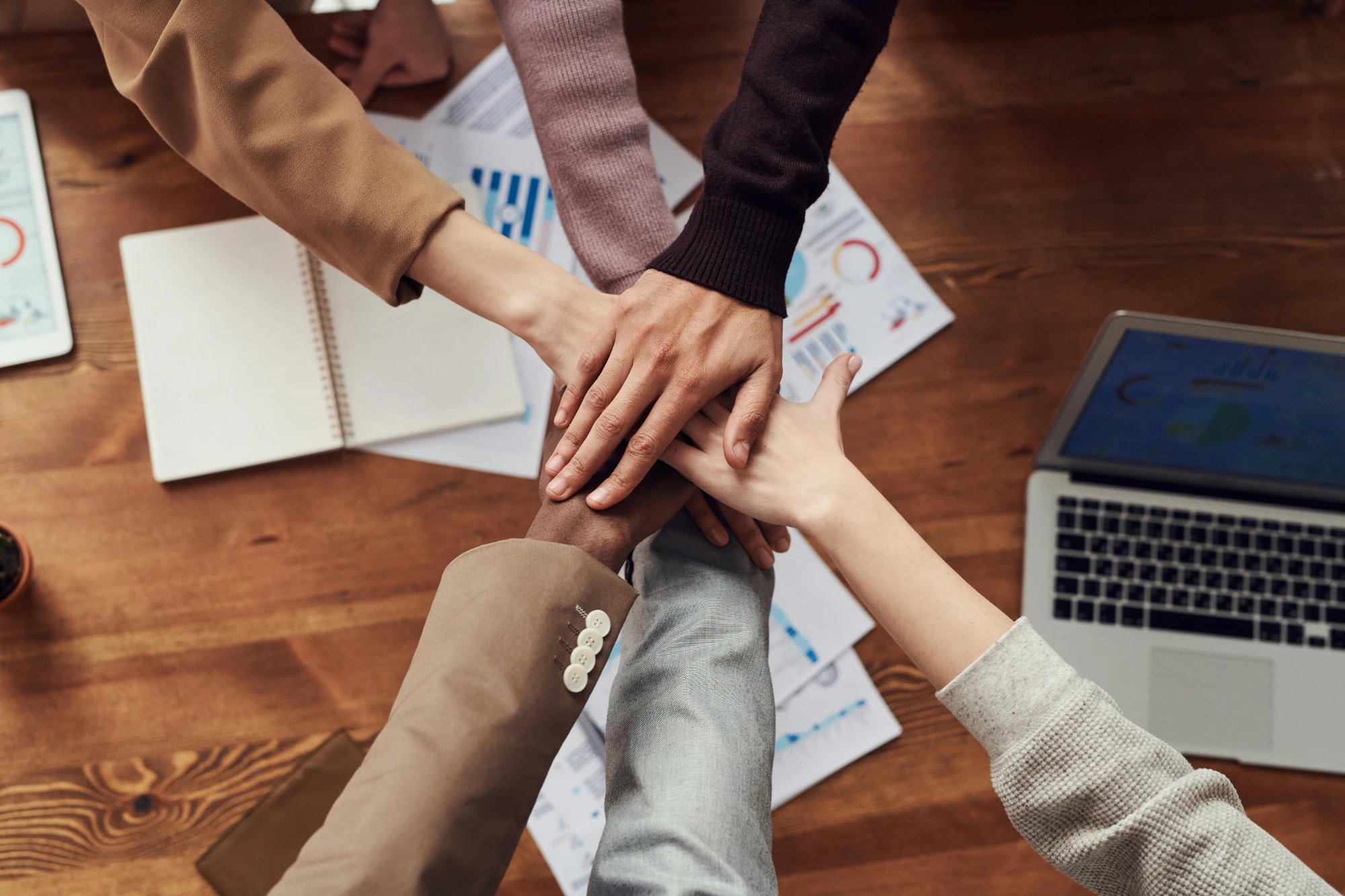 A diverse project team placing their hands together around a shared workspace.